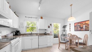 Une cuisine moderne avec des meubles blancs, un lave-vaisselle et un coin repas comprenant des chaises et une table en bois.