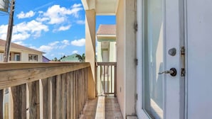 A balcony with a wooden railing, a glass door, and a view of a neighboring building. - Beachfront South Padre Retreat w/ Balcony & Pool (South Padre Island)