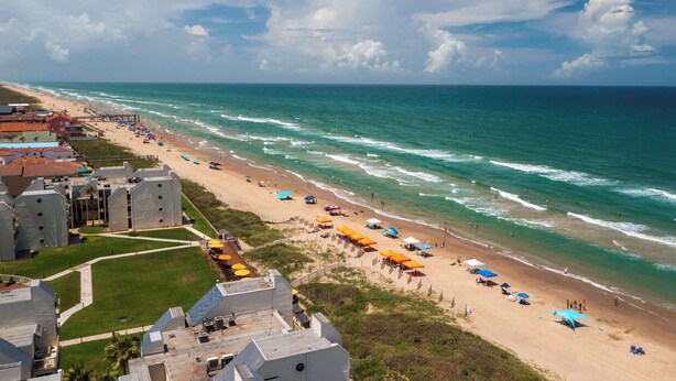 A beach with umbrellas and people, a building with a flat roof, and a clear sky. - Beachfront South Padre Retreat w/ Balcony & Pool (South Padre Island)