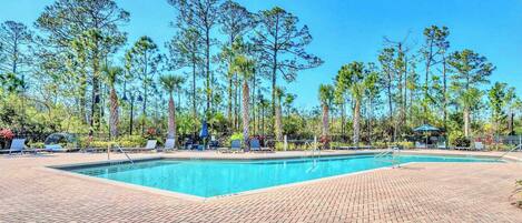 A rectangular swimming pool with a brick deck, surrounded by tall trees and lounge chairs.