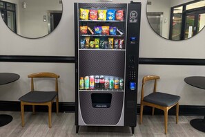A vending machine with snacks and drinks, two wooden chairs, and a mirror on the wall. - Upstay - Large Condo Near Disney w Pool and Gym (Winter Garden)