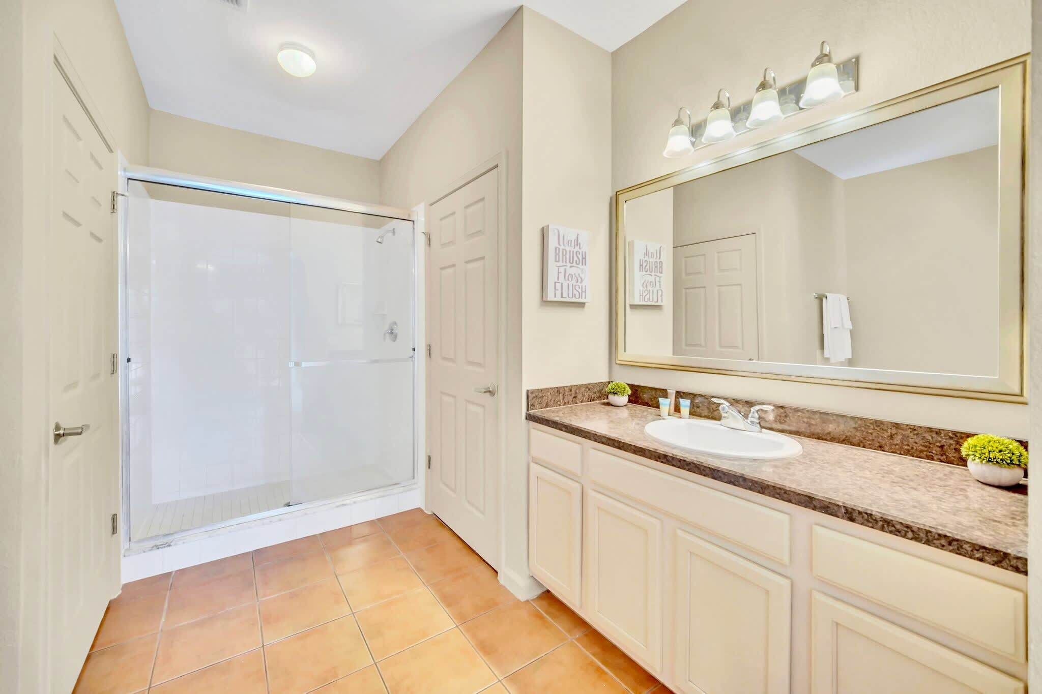 A bathroom with a glass shower enclosure, a sink with a vanity, and a large mirror with lights.