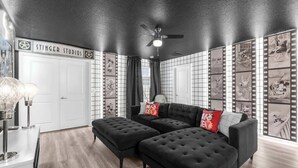 Una habitación con techo negro, sofá negro, puerta blanca y una pared decorada con motivos de fotogramas de cine.