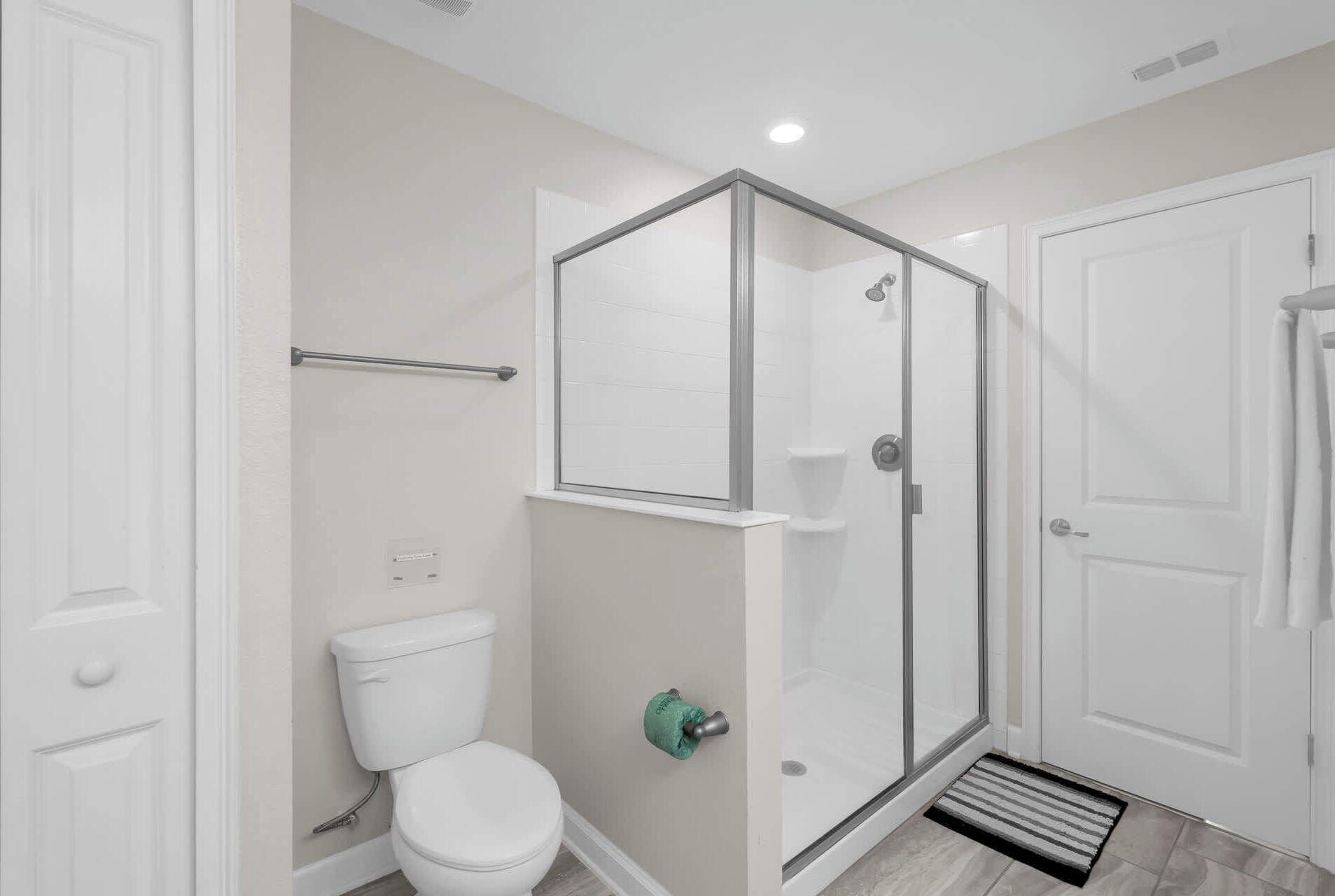 Een badkamer met een toilet, een douche met glazen deur en een deur met handdoekhouder.