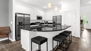 A modern kitchen with white cabinets, stainless steel appliances, a central island with bar stools, and pendant lighting. - Upstay: Ultimate Orlando Retreat w Pool & Hot Tub (Kissimmee)