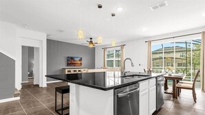 A modern kitchen with a central island, a dining area with a view, and a staircase leading to another level. - Upstay: Ultimate Orlando Retreat w Pool & Hot Tub (Kissimmee)