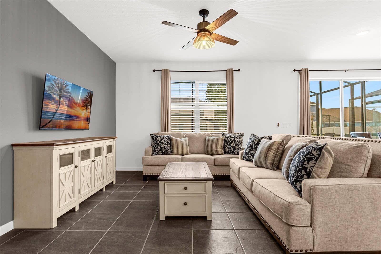 A living room with a beige sofa, a wooden coffee table, a cabinet, and a ceiling fan.