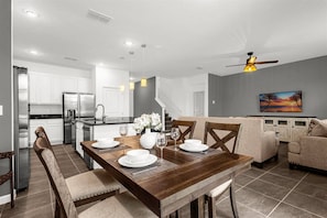A modern kitchen with white cabinets, a stainless steel refrigerator, and a dining area with a wooden table set for four. - Upstay: Ultimate Orlando Retreat w Pool & Hot Tub (Kissimmee)