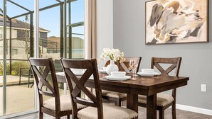 A dining area with a large table, four wooden chairs, and a vase of white flowers. - Upstay: Ultimate Orlando Retreat w Pool & Hot Tub (Kissimmee)