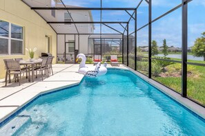 A swimming pool with a swan float, outdoor seating, and a view of a lake. - Upstay - Mansion w/ Kids Theme Rooms, Pool, Cinema (Kissimmee)