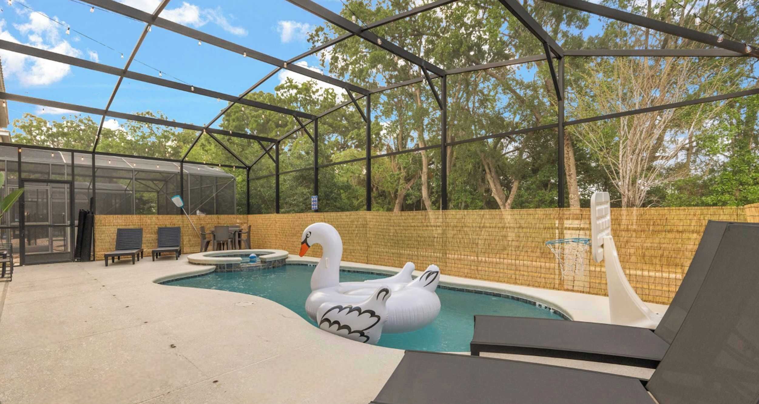 A covered outdoor swimming pool with a swan float, lounge chairs, and a basketball hoop.