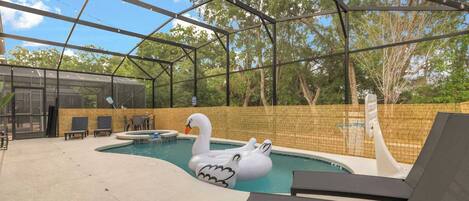 A covered outdoor swimming pool with a swan float, lounge chairs, and a basketball hoop.
