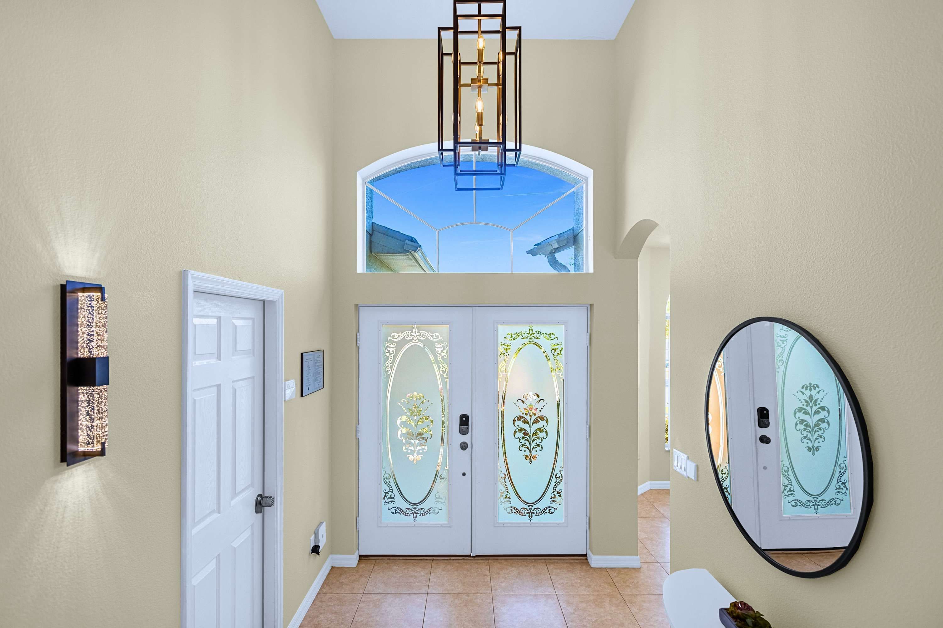 A hallway with a white door, a wall-mounted light fixture, and a large mirror.
