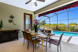 Un patio couvert avec une piscine, une table à manger, des chaises et un ventilateur de plafond.