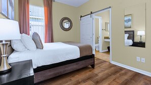 A hotel room with a bed, a bedside table, a lamp, a mirror, and a door leading to a bathroom. - Upstay: Crystal Cove Resort Villa w/ Pool & Games (Kissimmee)