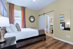 A hotel room with a bed, a bedside table, a lamp, a mirror, and a door leading to a bathroom. - Upstay: Crystal Cove Resort Villa w/ Pool & Games (Kissimmee)
