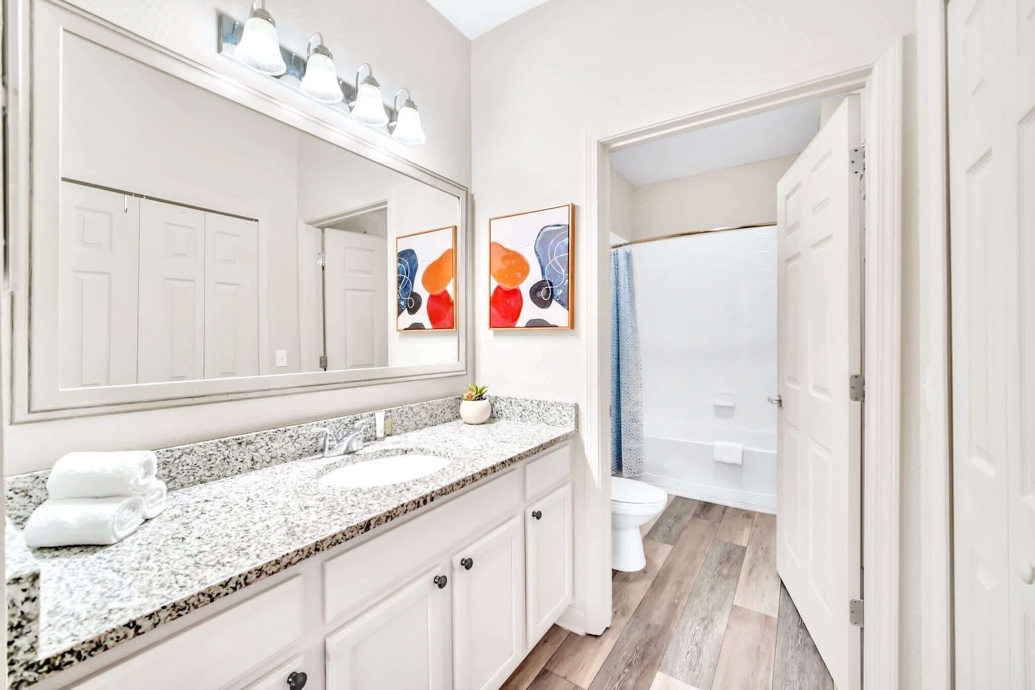 A bathroom with a granite countertop, two sinks, a large mirror, and a shower area.
