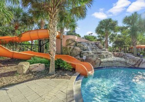 A swimming pool with a water slide, palm trees, and a rocky waterfall feature. - Pool/hot Tub Heating Included, Epic Games Room! (Davenport)