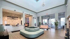 A hotel lobby with a reception desk, a curved seating area, and large windows offering views of the outdoors. - Upstay: Family Retreat w Pool, Cinema & Games Room (Clermont)