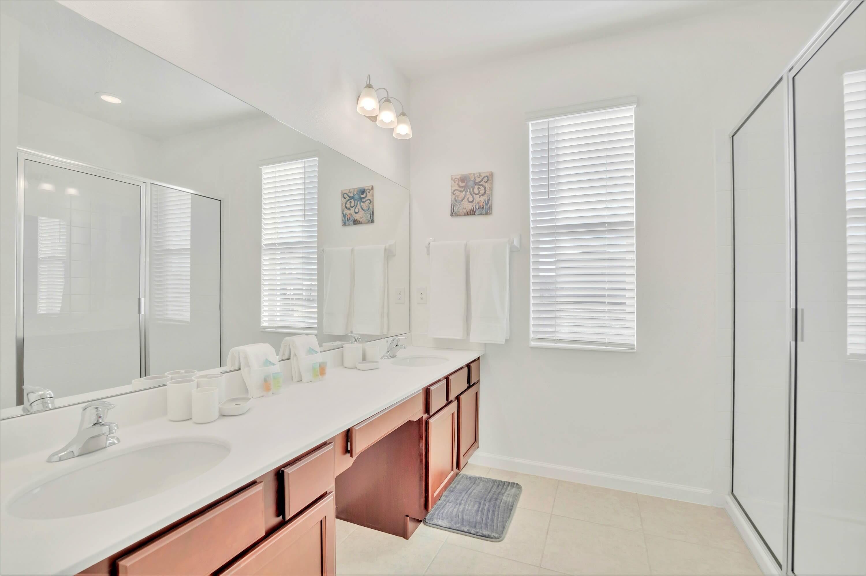A modern bathroom with a large mirror, two sinks, and a walk-in shower.