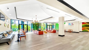 Eine geräumige Lobby mit hoher Decke, großen Fenstern und verschiedenen Sitzbereichen, darunter Sofas und Tische.