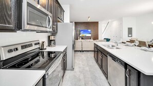 A modern kitchen with a built-in oven, microwave, and dishwasher. There is a large island with a sink and a seating area in the background. - Solara Resort Home With Private Pool Near Disney (Kissimmee)