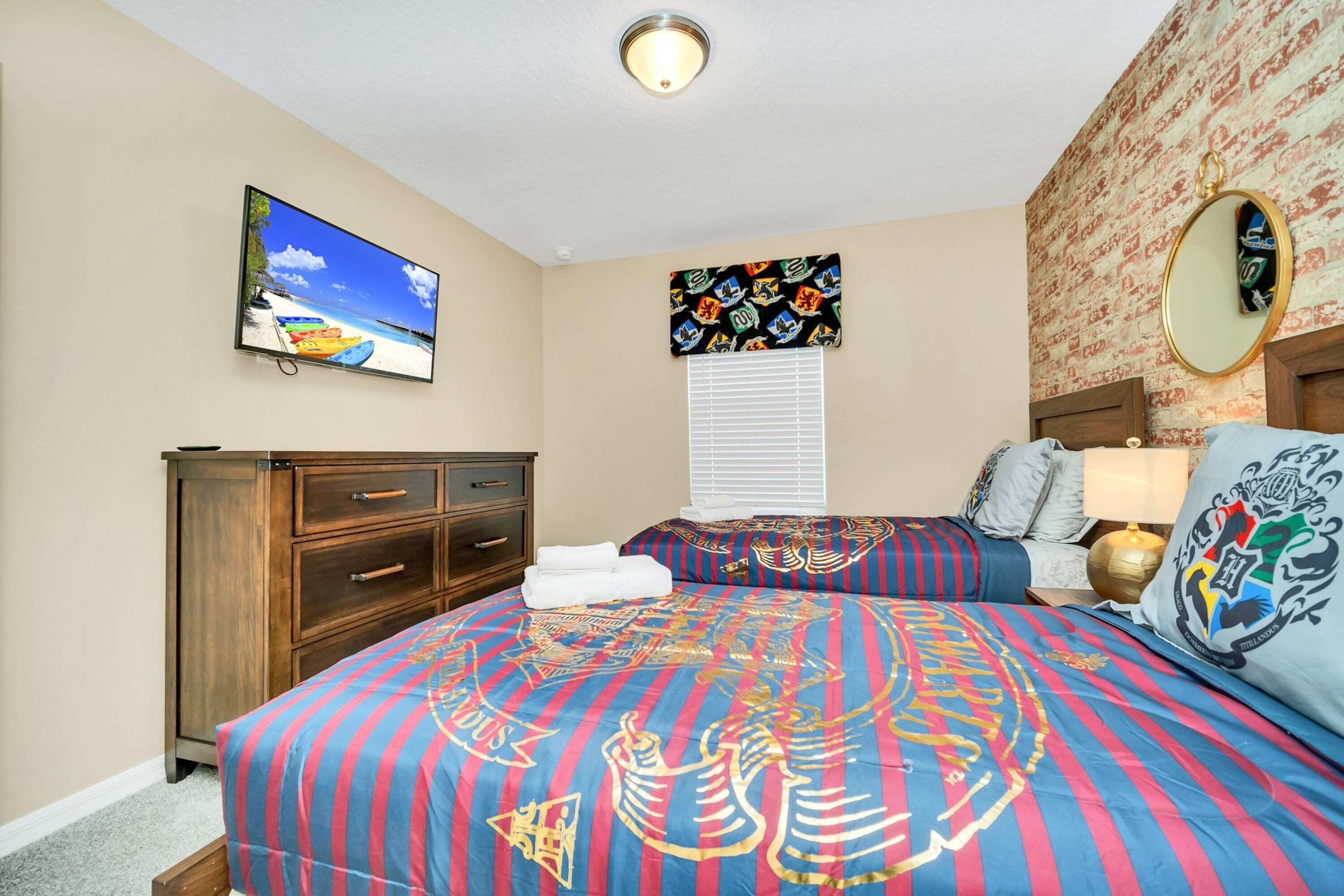 Een slaapkamer met een groot bed, een televisie aan de muur, een dressoir en een raam met zonwering.