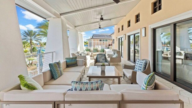 A covered outdoor seating area with sofas and chairs, large windows, and a ceiling fan. - Solara Resort Home With Private Pool Near Disney (Kissimmee)
