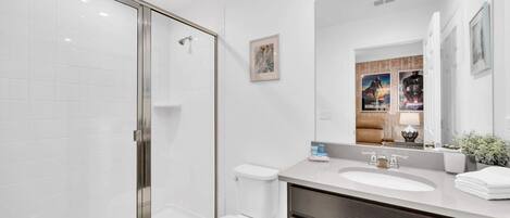 Une salle de bain moderne avec une douche à parois de verre, des toilettes blanches, un meuble-lavabo avec un grand miroir et un évier.