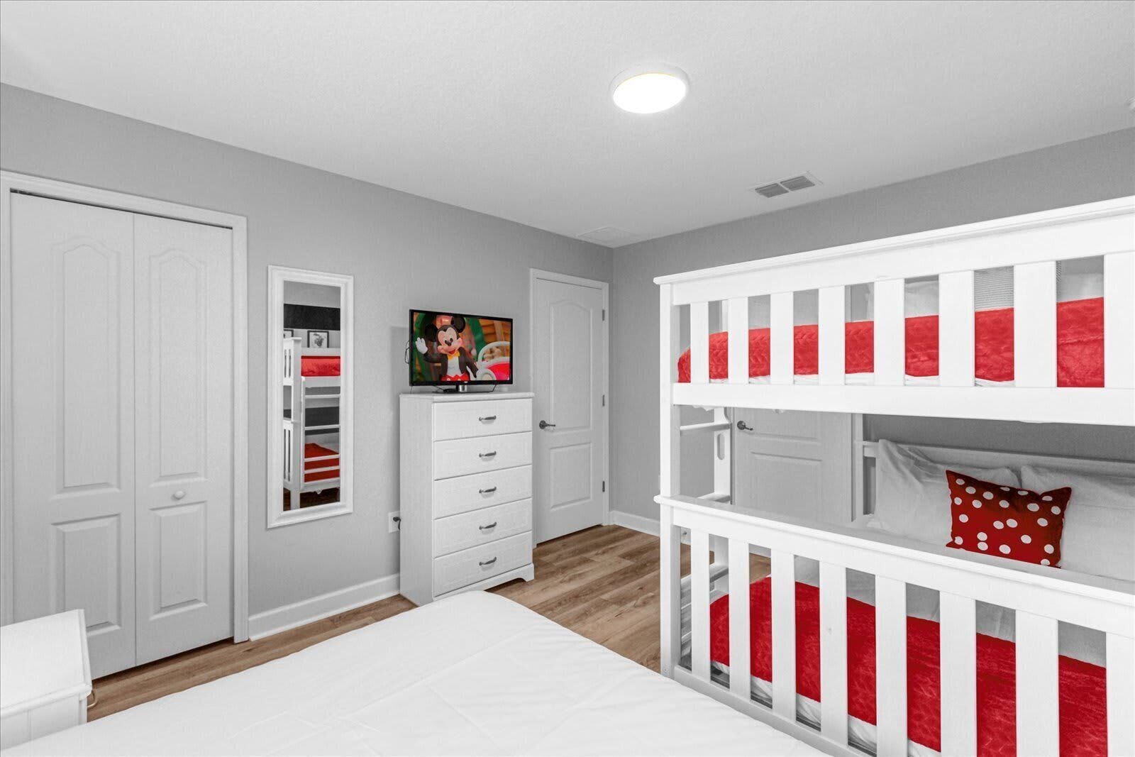 A bedroom with a bunk bed, a dresser, a television, and a window with a view of the outside.