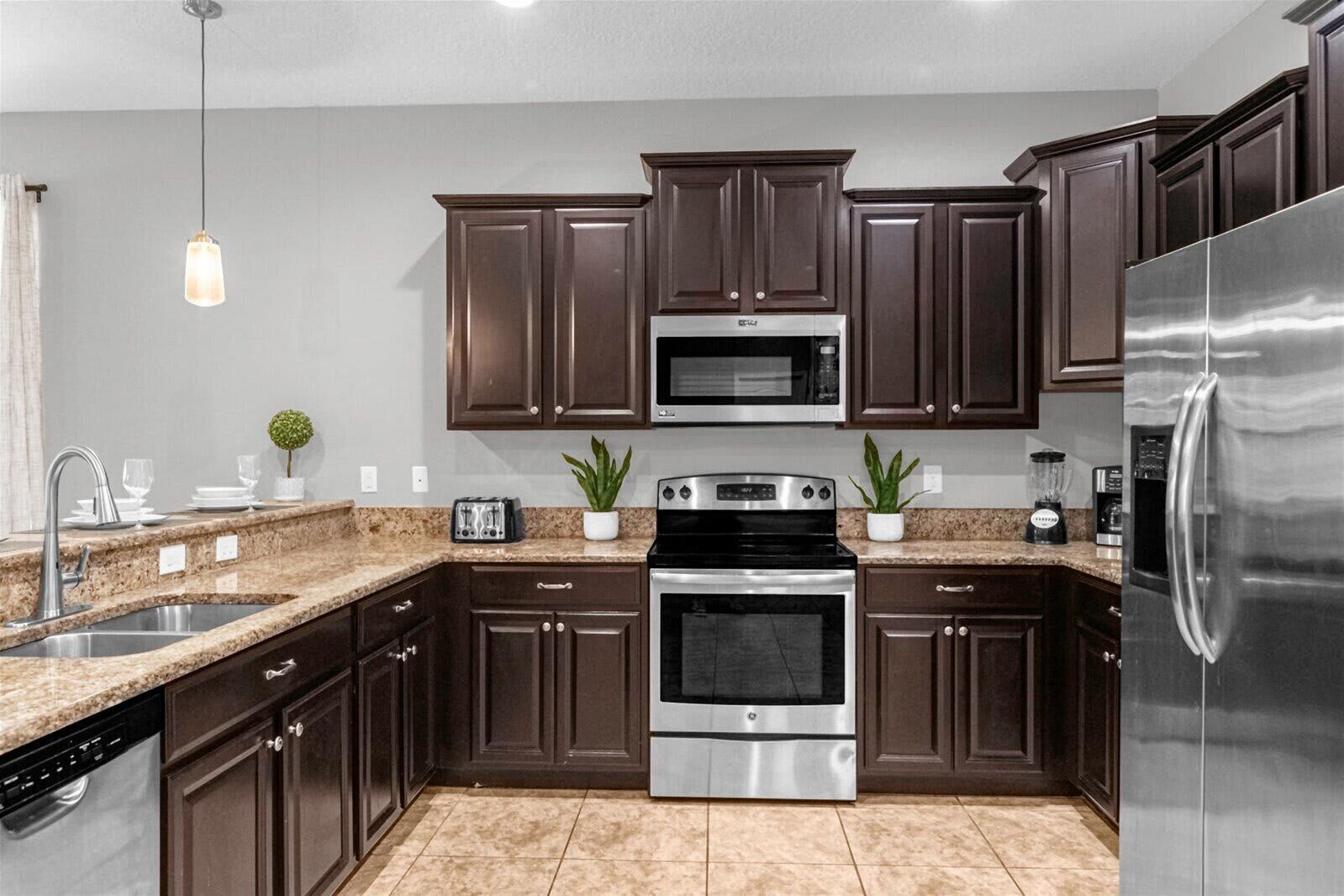 A modern kitchen with dark wood cabinets, stainless steel appliances, granite countertops, and a hanging pendant light.