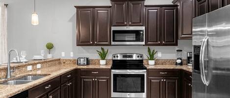A modern kitchen with dark wood cabinets, stainless steel appliances, granite countertops, and a hanging pendant light.
