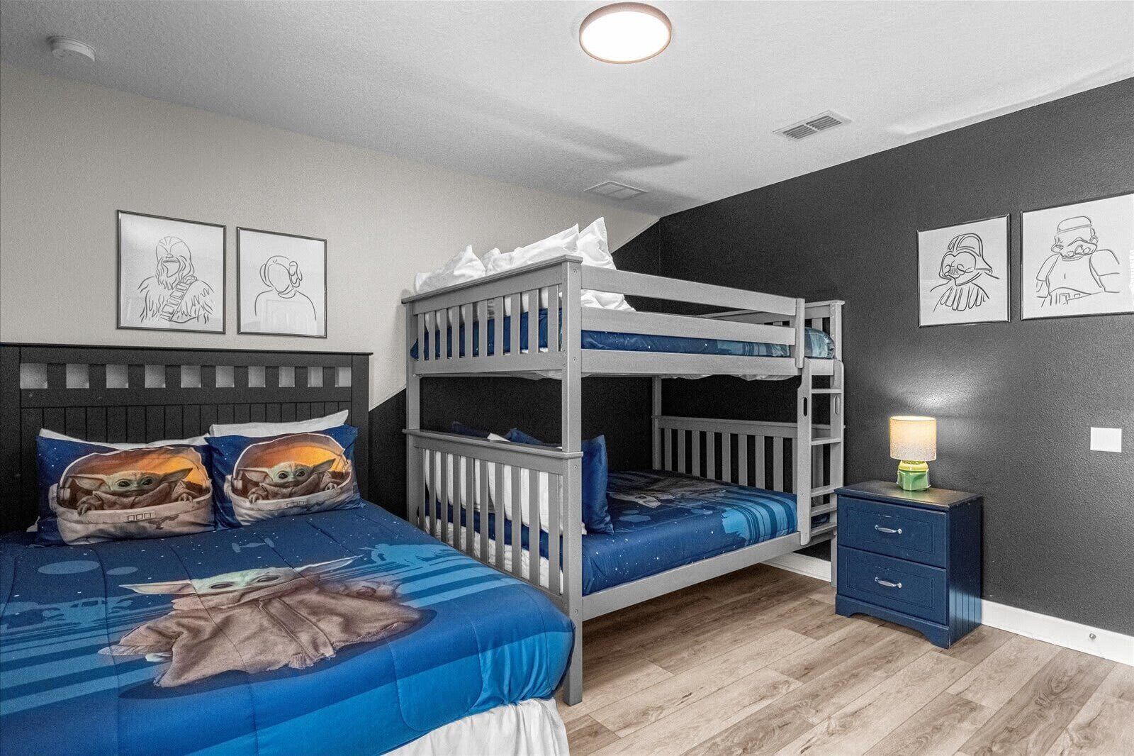 Une chambre avec un lit superposé, une couverture bleue, une table de chevet avec une lampe et des œuvres d’art encadrées accrochées aux murs.