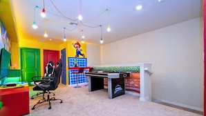 Quarto com escrivaninha, cadeiras, mesa de jogos e decorações vibrantes nas paredes.