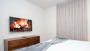 Quarto com cama, cômoda de madeira, pintura de uma lareira e janela com cortinas.