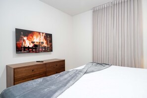A bedroom with a bed, a wooden dresser, a painting of a fire, and a window with curtains. - Upstay Family Fun 5BR Retreat w Pool & Games Room (Clermont)