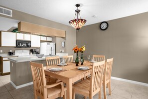 A modern kitchen with a central island, wooden chairs, and a dining table set for four. - Upstay Sunny Home w Private Patio Near Disney (Kissimmee)