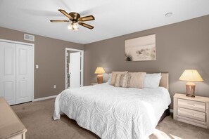 A bedroom with a large bed, two bedside lamps, a ceiling fan, a door, and a wall-mounted picture. - Upstay Sunny Home w Private Patio Near Disney (Kissimmee)