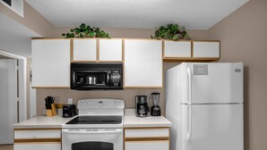 A compact kitchen with white appliances, including a stove, microwave, and refrigerator, with wooden accents and green plants on the countertop. - Upstay Sunny Home w Private Patio Near Disney (Kissimmee)