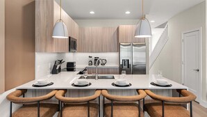 Een moderne keuken met een centraal eiland, roestvrijstalen apparatuur en hanglampen.