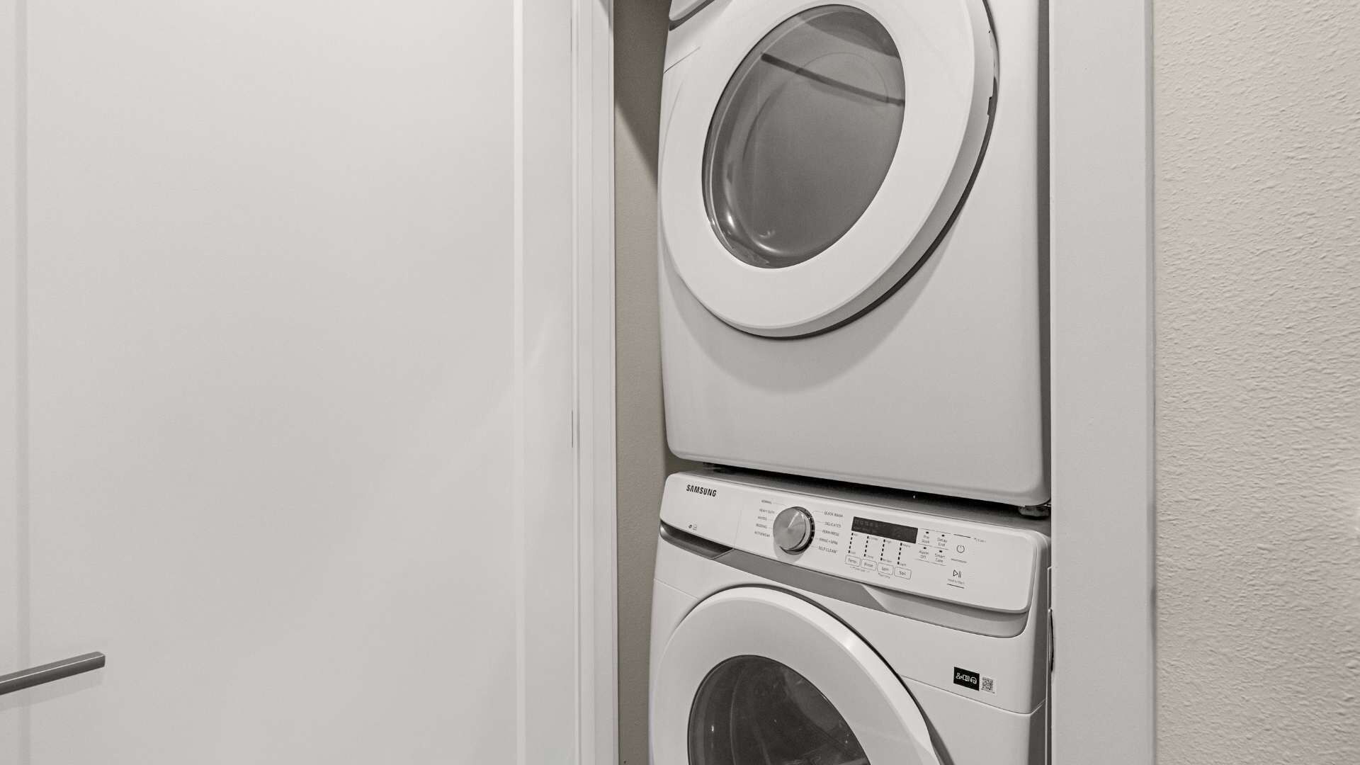 A stacked washer and dryer unit in a room with a plain white door and wall.