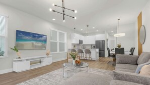 A modern living room with a gray sofa, a glass coffee table, and a large painting of a beach scene.