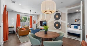 A modern living room with a round wooden table, two sofas, a TV, and a guitar on the wall. - Eclectic Group Getaway With Pool, Patio & Fire Pit (Austin)