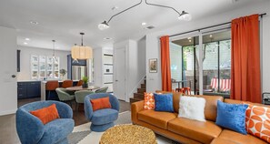A modern living room with a brown sofa, blue armchairs, and orange curtains. - Eclectic Group Getaway With Pool, Patio & Fire Pit (Austin)