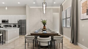 Une cuisine moderne avec des meubles blancs, des appareils en acier inoxydable et un coin repas doté d’une longue table pouvant accueillir six personnes.