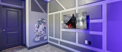 A hallway with a grey door, a wall-mounted Star Wars-themed artwork, and a Star Wars character cutout.