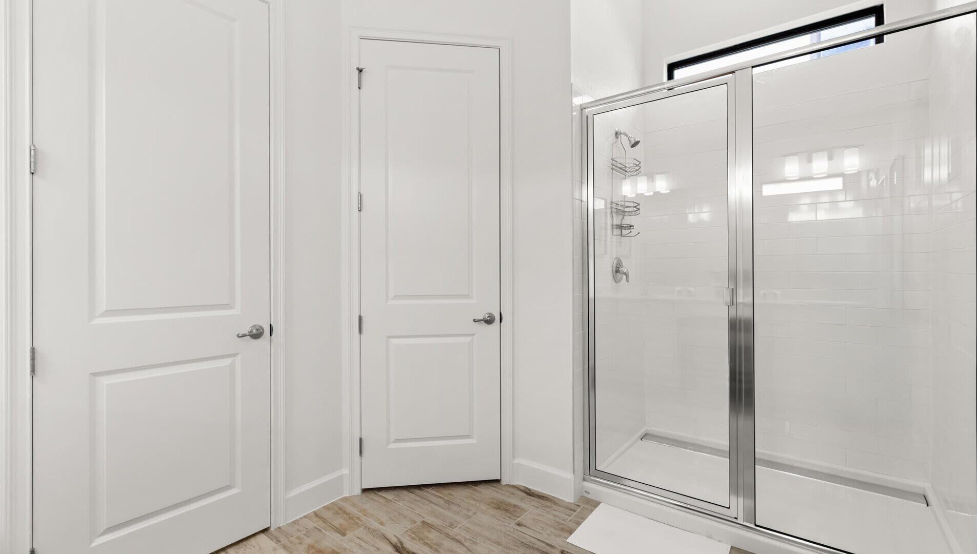 A bathroom with white doors, a glass shower enclosure, and a tiled floor.