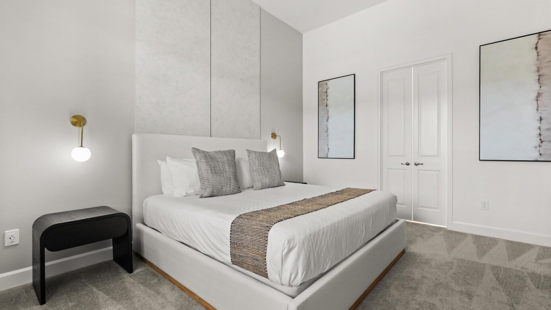 A modern bedroom with a large bed, bedside tables, and artwork on the walls.