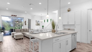 A modern kitchen with white cabinetry, a large island with a sink, and pendant lighting. - Upstay Family Getaway With Pool Near Disney (Davenport)