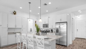 A modern kitchen with white cabinets, stainless steel appliances, and a central island with bar stools. - Upstay Family Getaway With Pool Near Disney (Davenport)